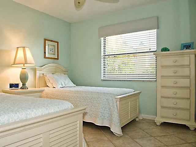Tiled guest bedroom with 2 twin beds, TV and DVD player with ceiling fan.